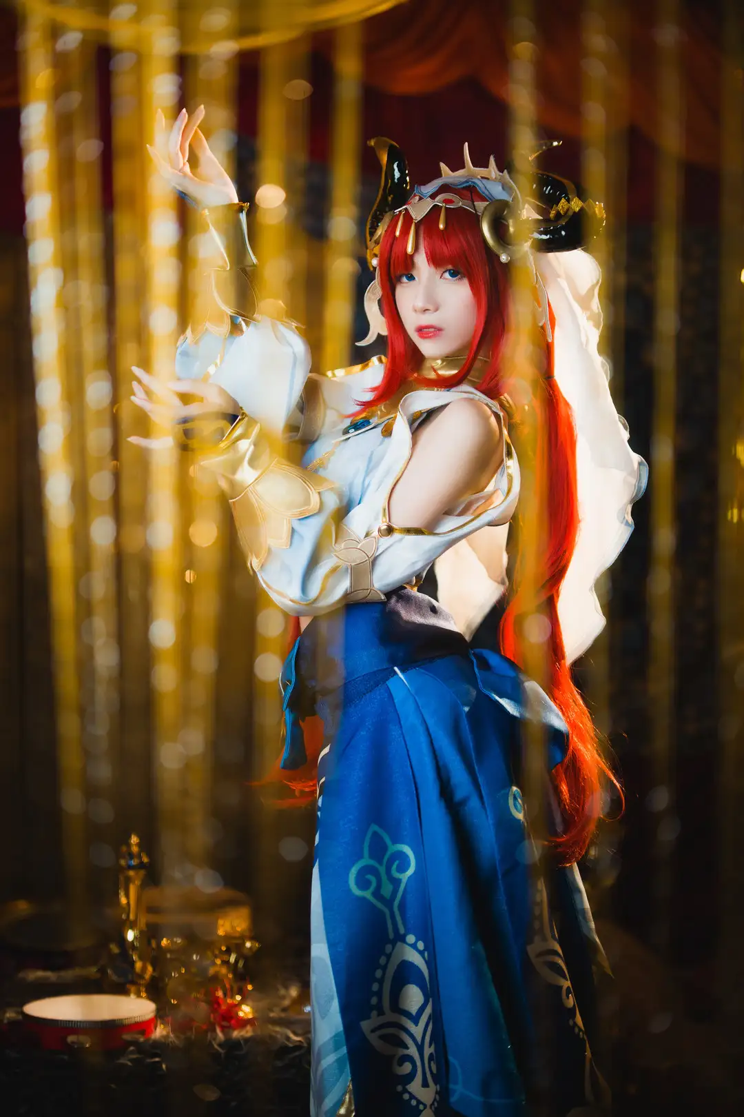 清青琴玖 原神妮露cos 金色头冠与黑色犄角,白蓝短上衣配深蓝印花长裙,金色帘幕前的舞蹈姿态 清青琴玖 原神妮露cos 金色头冠与黑色犄角,白蓝短上衣配深蓝印花长裙,金色帘幕前的舞蹈姿态